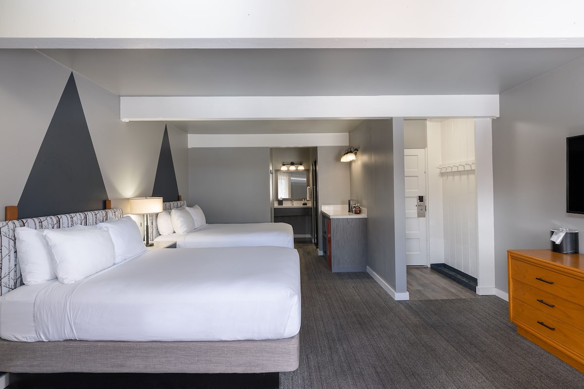 A hotel room with two beds, a desk, a dresser, and a television.