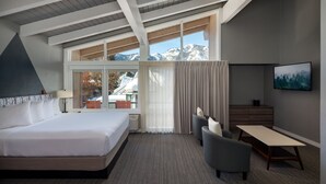 A modern hotel room with a large bed, a desk, and a view of mountains through the windows. - Tamarack Lodge Sun Valley (Ketchum)