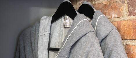Two grey hoodies hanging on a wooden rack against a brick wall.
