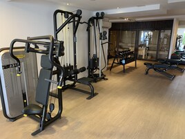 Un gimnasio con diferentes máquinas de ejercicio, una banca y un estante con mancuernas.
