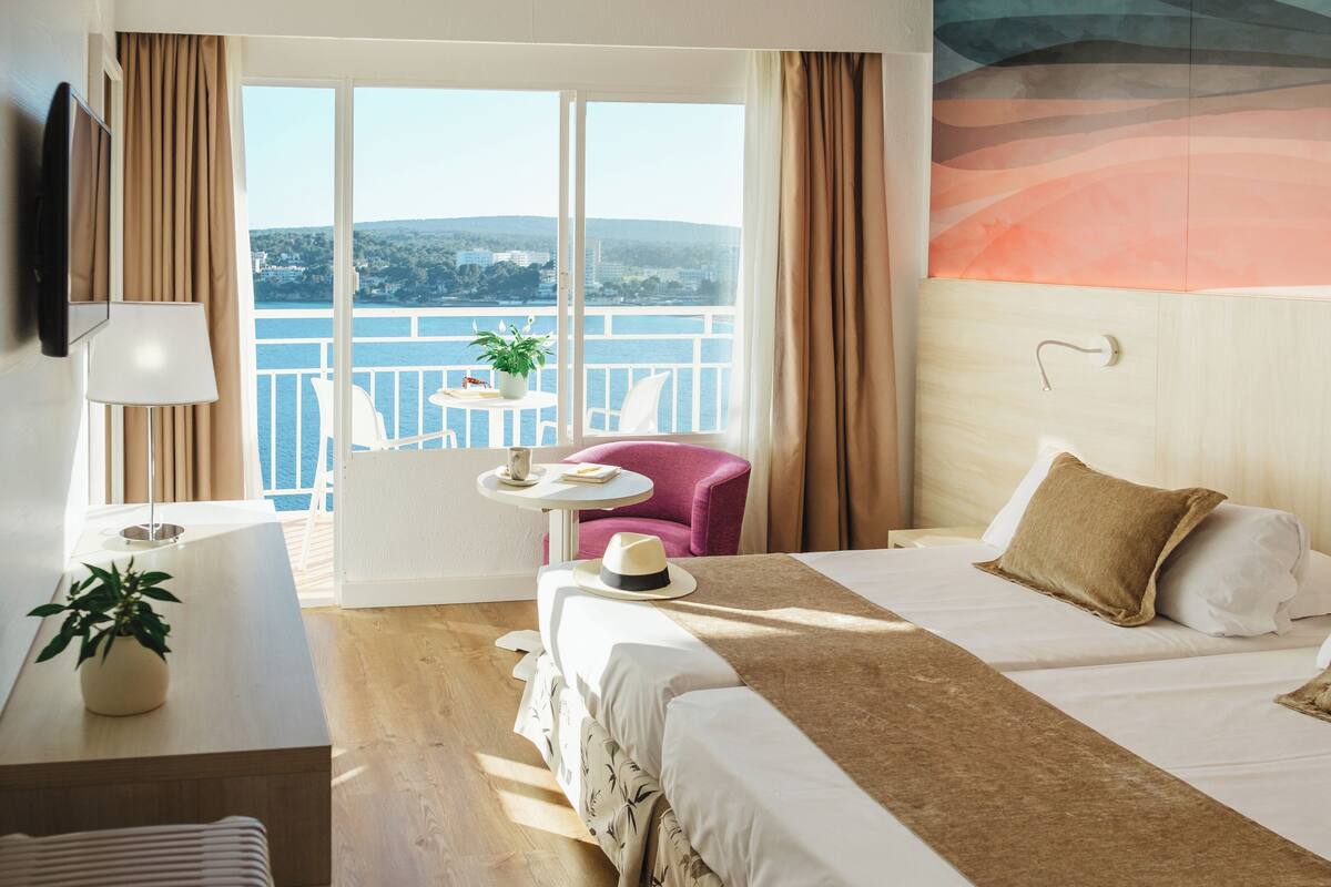 Habitación de hotel con cama, una silla, una mesita con una planta y vista al mar.