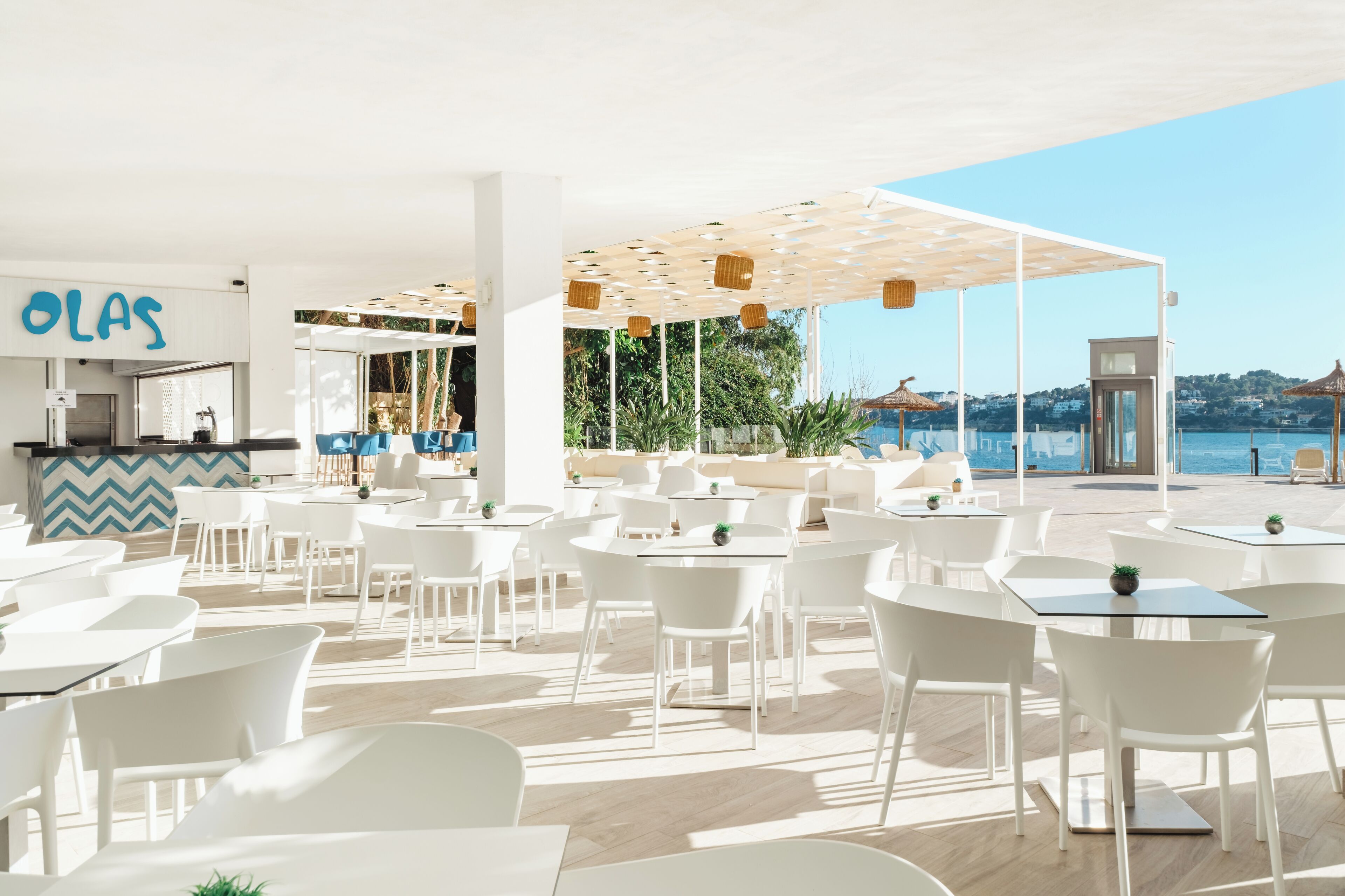 A modern outdoor dining area with white furniture and a view of the sea.