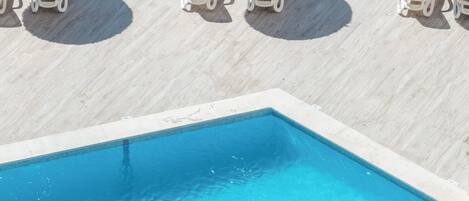 A poolside area with clear blue water, lounge chairs, and thatched umbrellas.