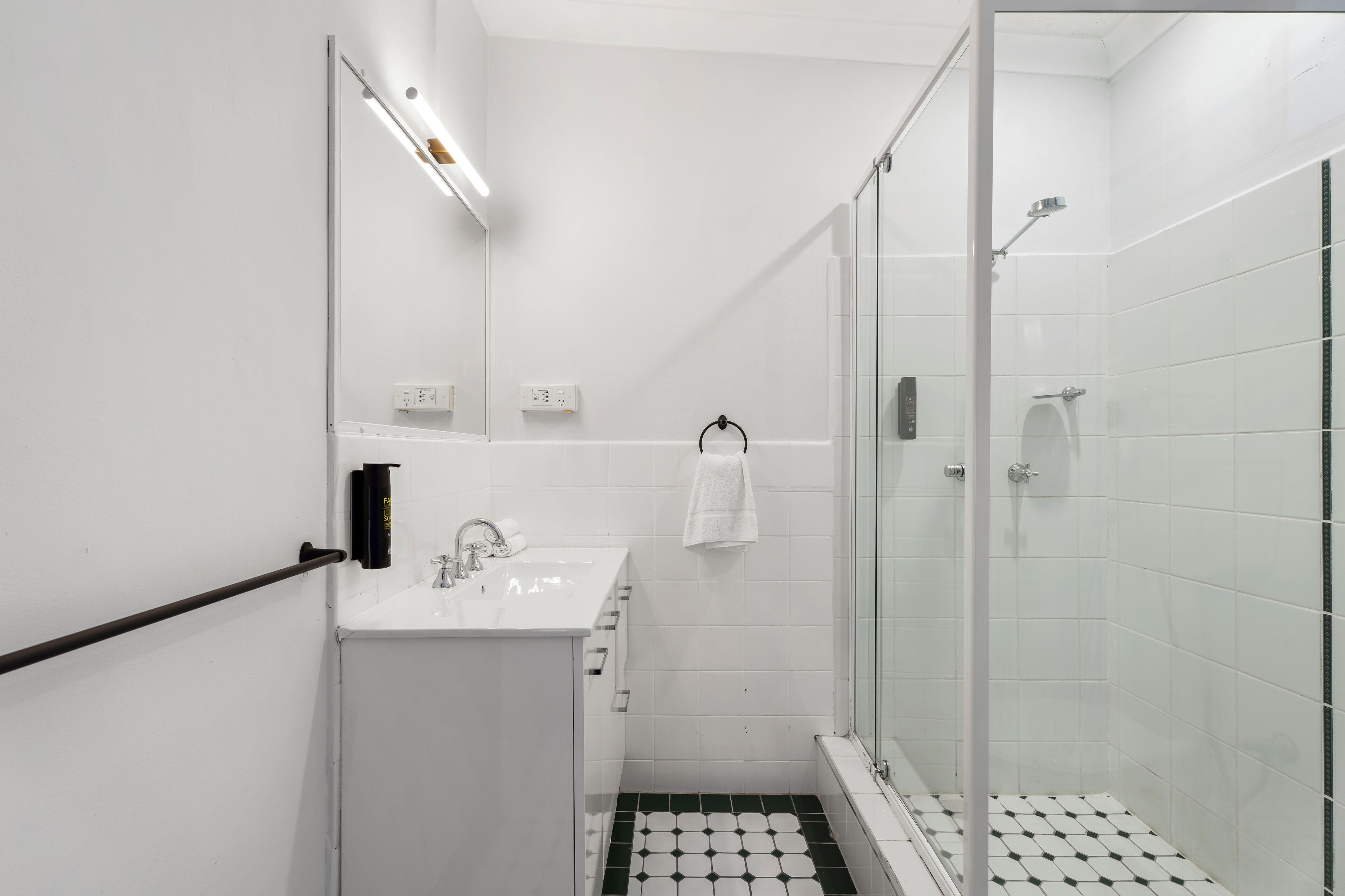Um banheiro moderno com box de vidro, pia branca e porta-toalhas preto.