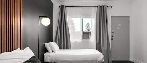 A modern hotel room with a bed, a bedside table, a lamp, and a window with curtains.