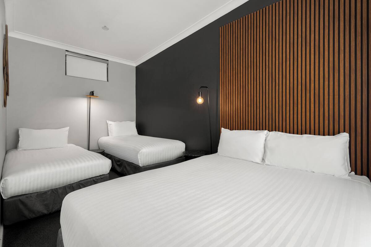 A hotel room with three beds, a modern design, and a wooden accent wall.