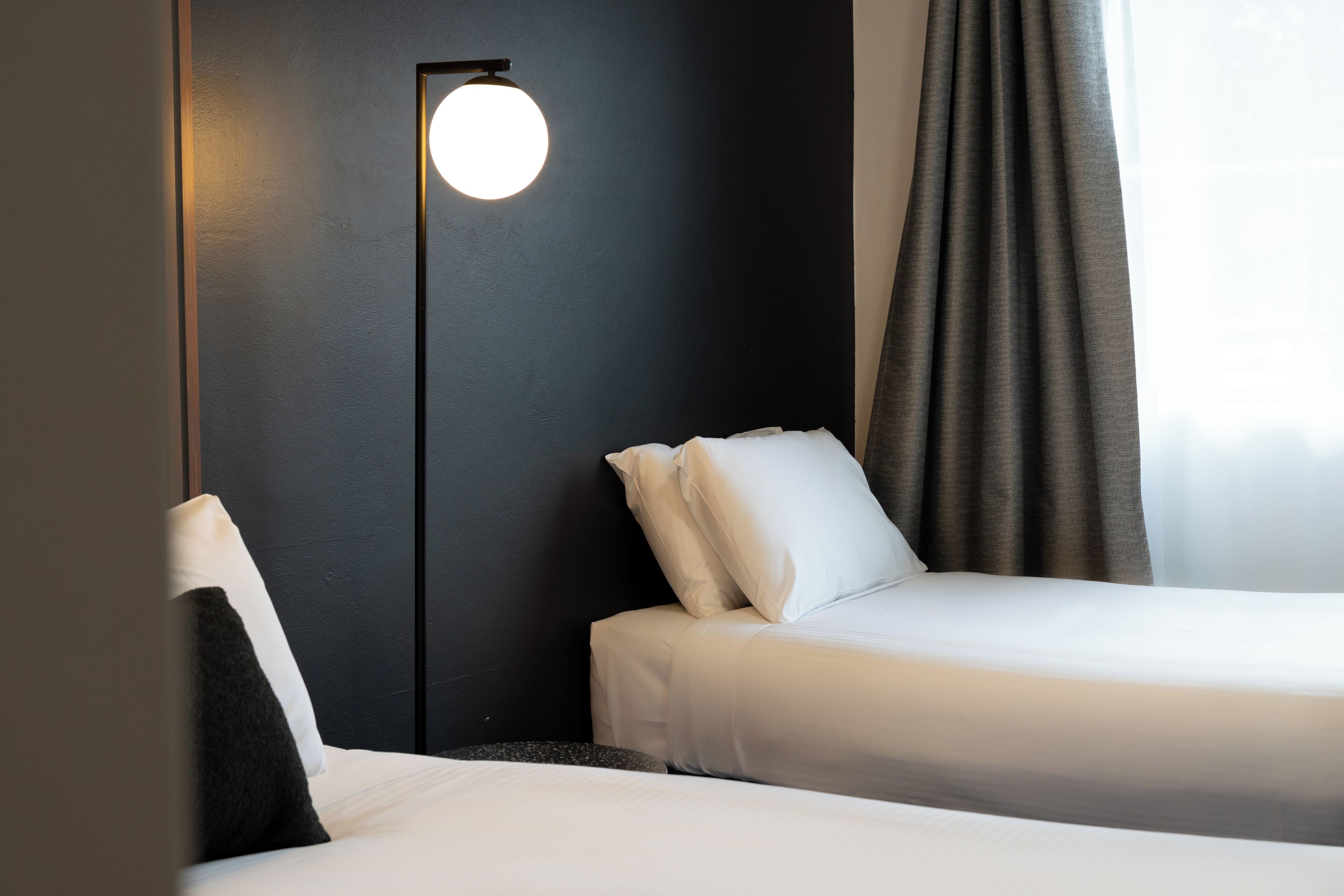 A hotel room with two beds, a wall-mounted light, and a window with curtains.