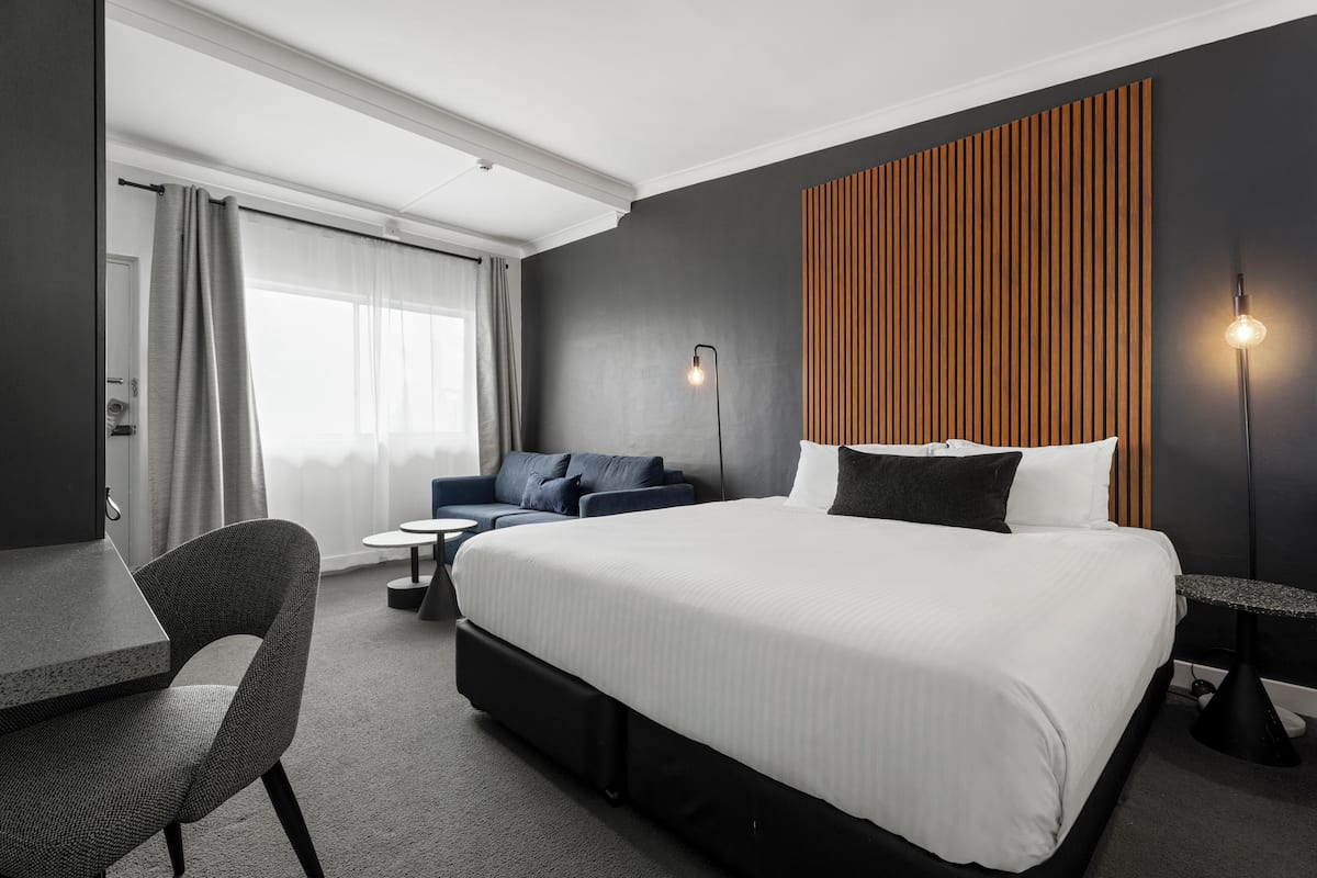 A modern hotel room with a large bed, a desk, a chair, and a sofa.