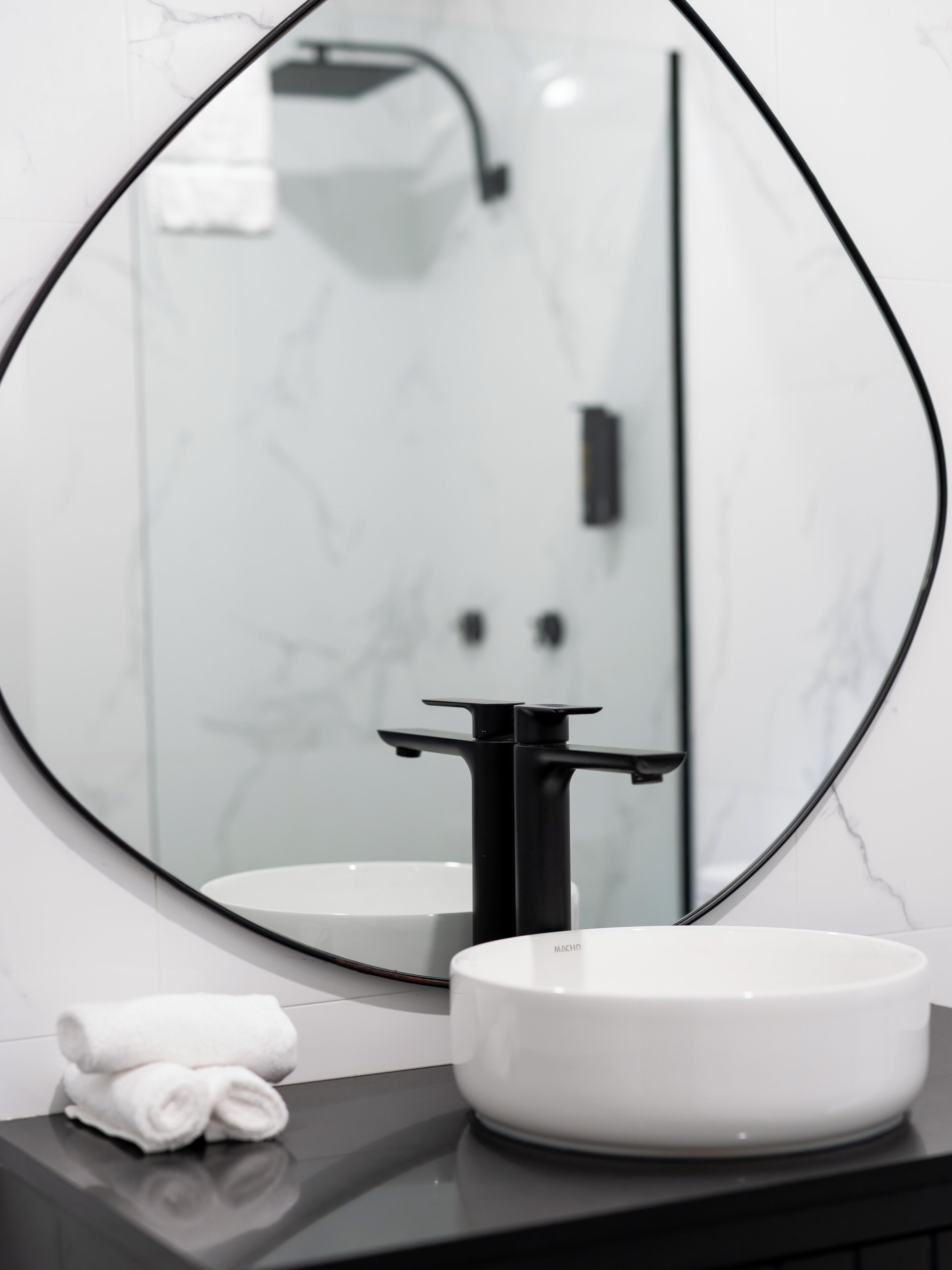Un baño con un espejo redondo, un lavamanos blanco y un grifo negro.