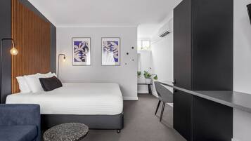 Ein modernes Hotelzimmer mit Bett, Schreibtisch, Stuhl, einem kleinen runden Tisch und zwei an der Wand befestigten Kunstwerken.