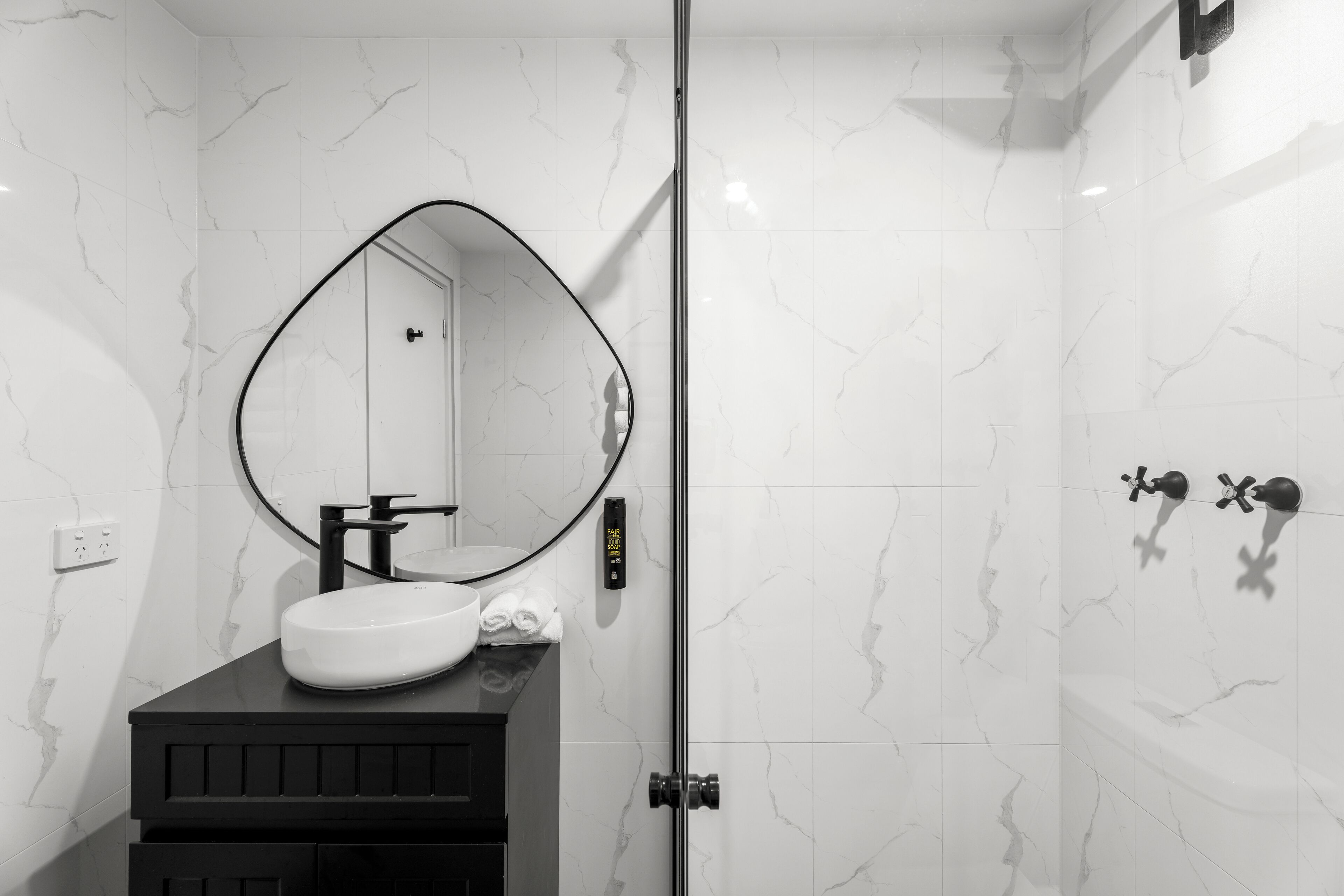 A bathroom with a white marble sink, a black vanity, a large mirror, and a shower with a glass door.