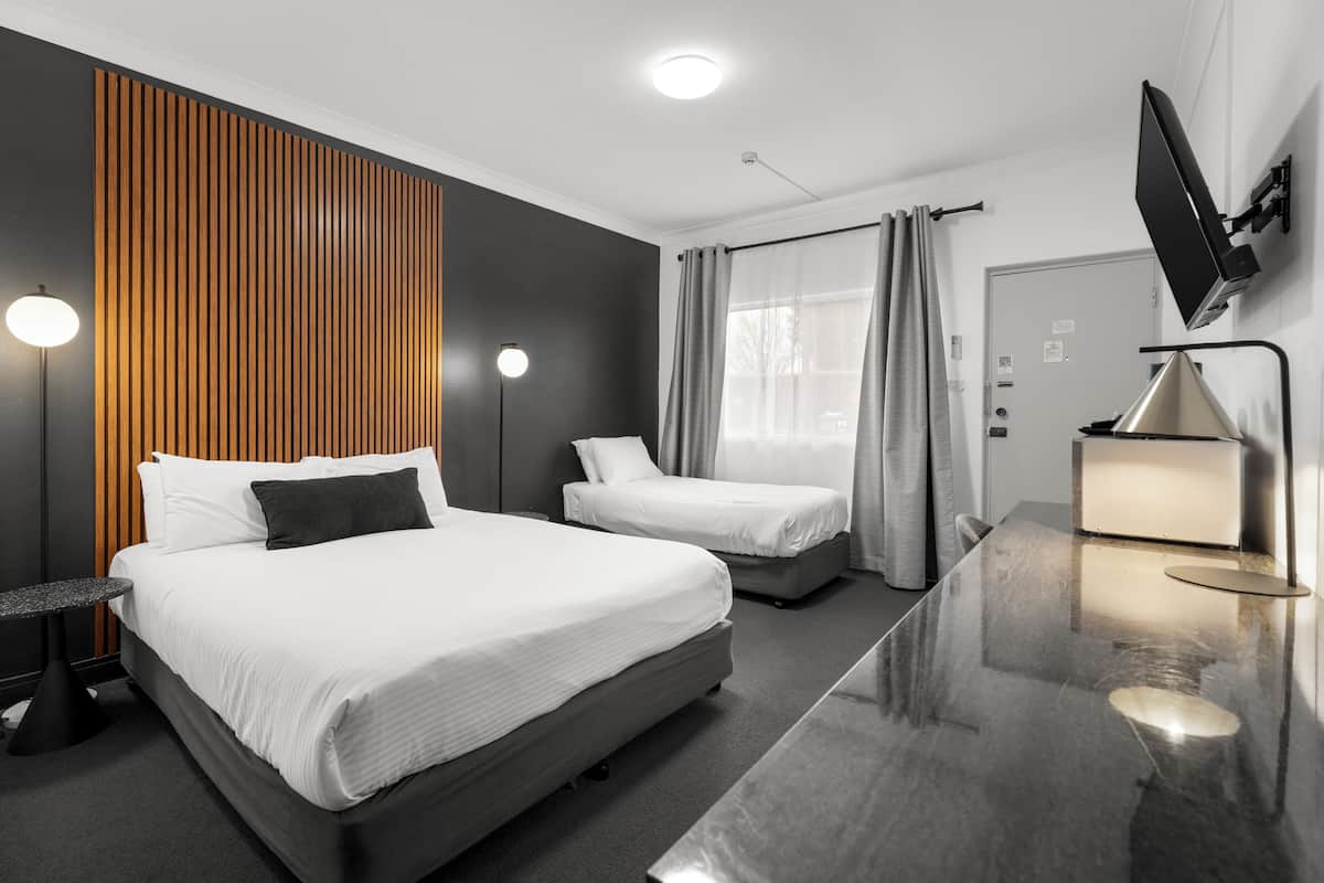 A hotel room with two beds, a desk, a TV, and a modern design with wooden paneling and a large window with curtains.