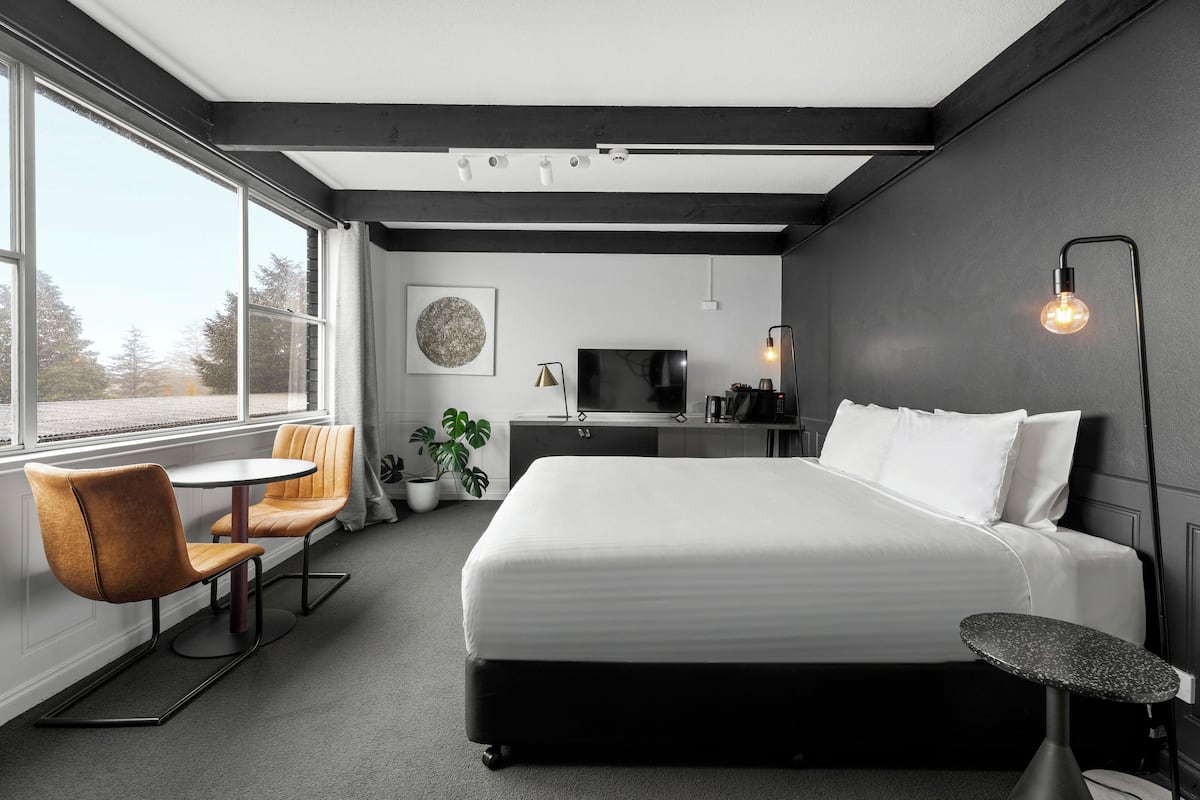 A modern bedroom with a large bed, a small round table, a sofa, and a TV.