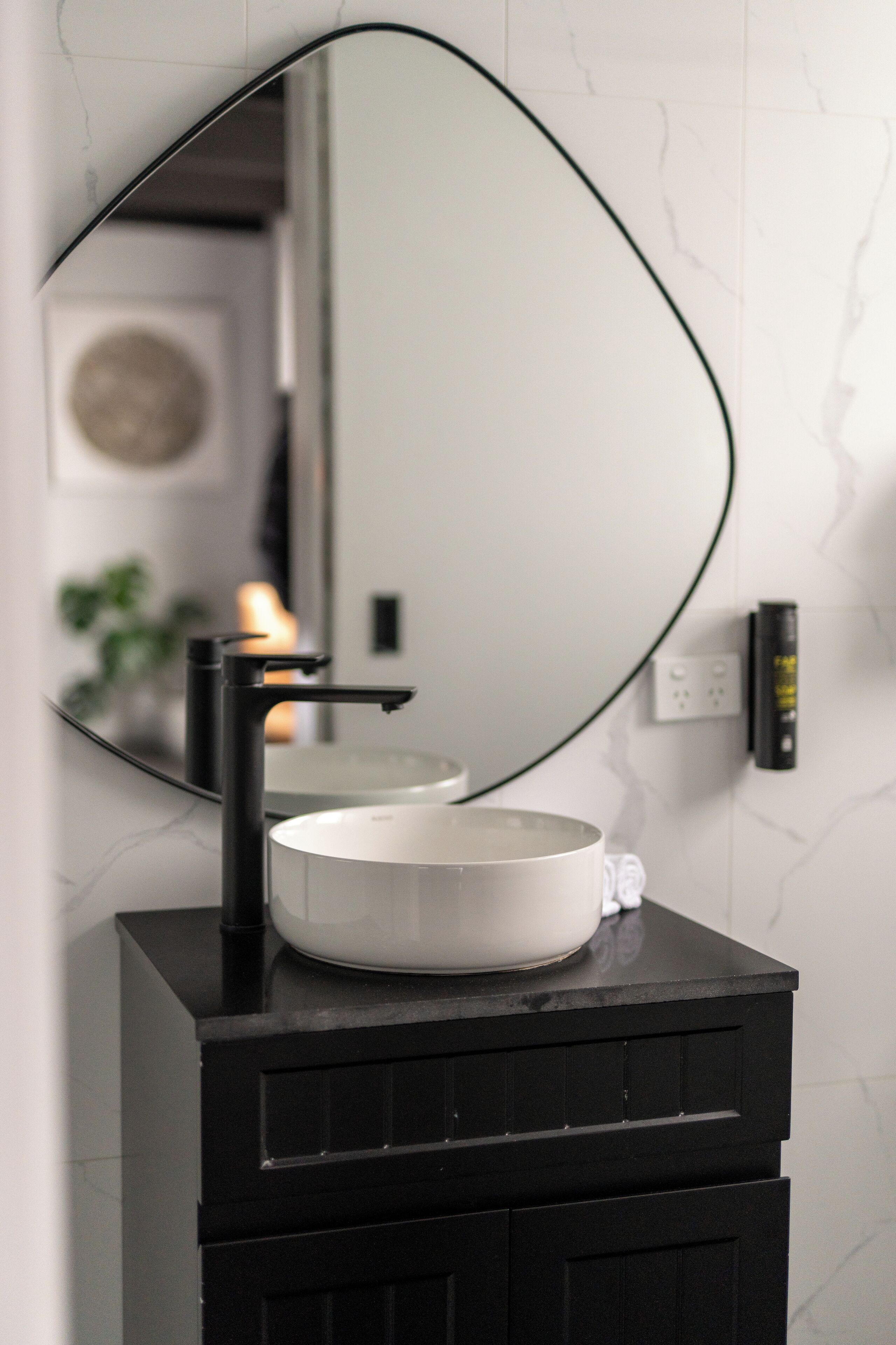 A modern bathroom vanity with a black sink, a large mirror, and a white marble backsplash.
