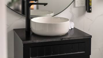 A modern bathroom vanity with a black sink, a large mirror, and a white marble backsplash.
