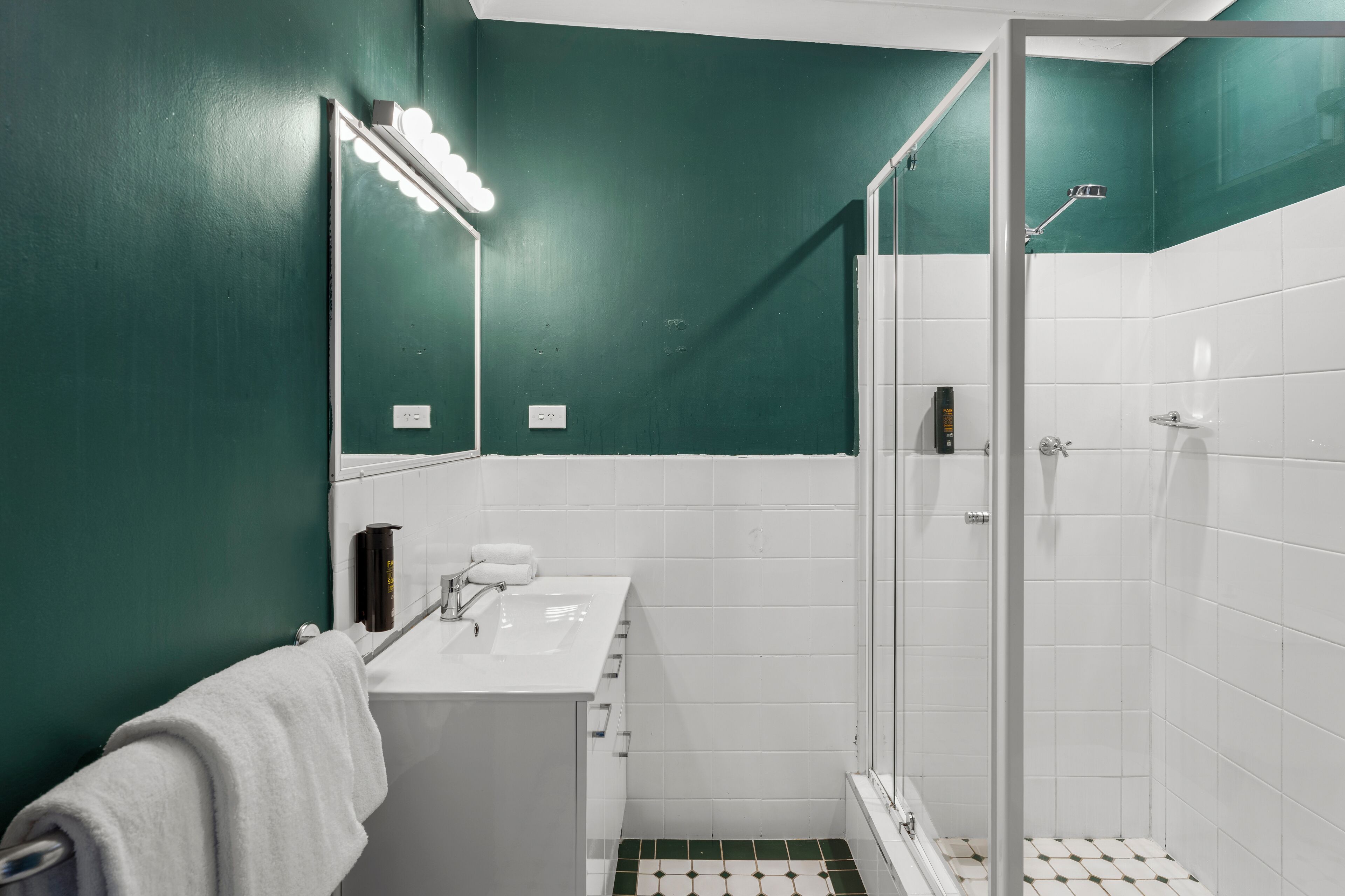 A bathroom with a white sink, green walls, and a shower area.