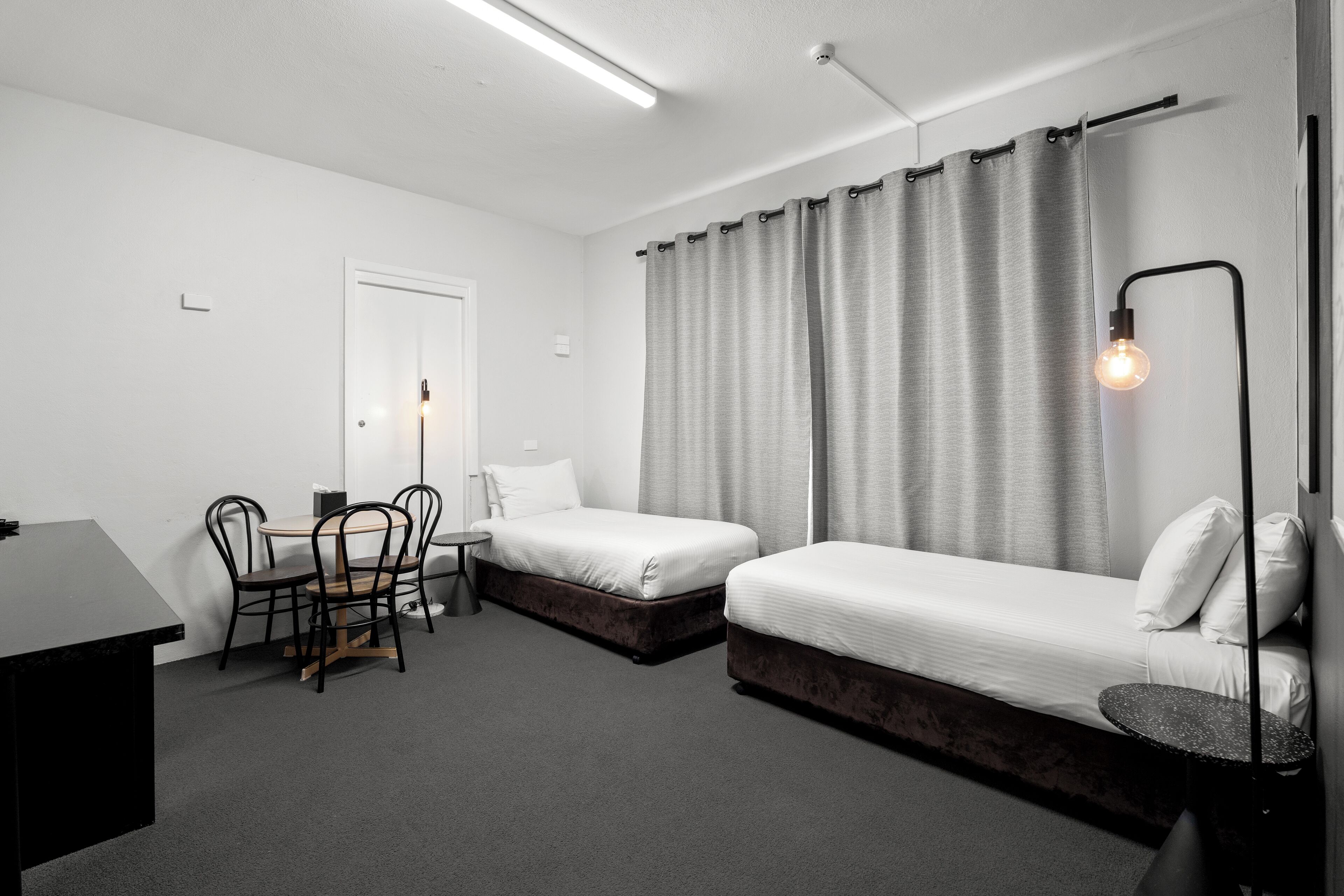 Una habitación de hotel moderna con dos camas individuales, una mesita, una silla y un escritorio.