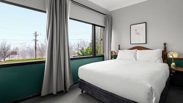 A hotel room with a large bed, a window with curtains, a framed picture on the wall, and a nightstand with a lamp.