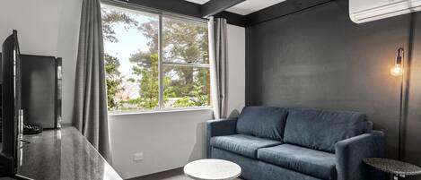 Una sala de estar moderna con un sofá azul oscuro, una mesita redonda y un televisor de pantalla plana.