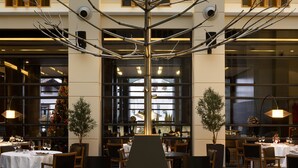 A modern interior with a central tree-like structure, large windows, and a dining area with tables and chairs. - Esperos Palace Luxury & Spa Hotel (Kastoria)