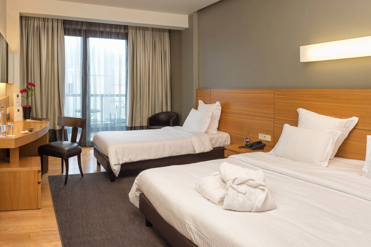 A hotel room with two beds, a desk, a chair, and a large window with curtains.