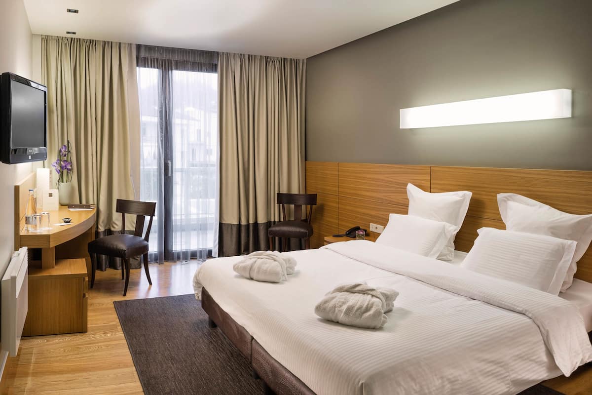 A hotel room with a bed, a desk, a chair, a TV, and a window with curtains.