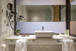 Un baño moderno con un espejo grande, un secador de pelo, un lavamanos y una planta en maceta.