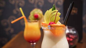 Two cocktails with garnishes and straws, a decorative glass, and a blurred background with a patterned wall.