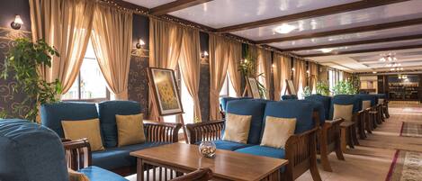 Un restaurante con sofás azules, mesas de madera y cortinas.