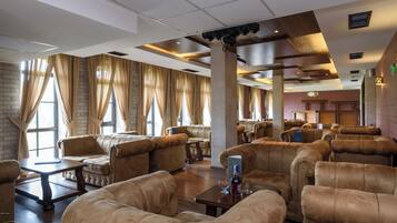 A spacious lounge area with leather sofas and armchairs, a wooden coffee table, and large windows with curtains.