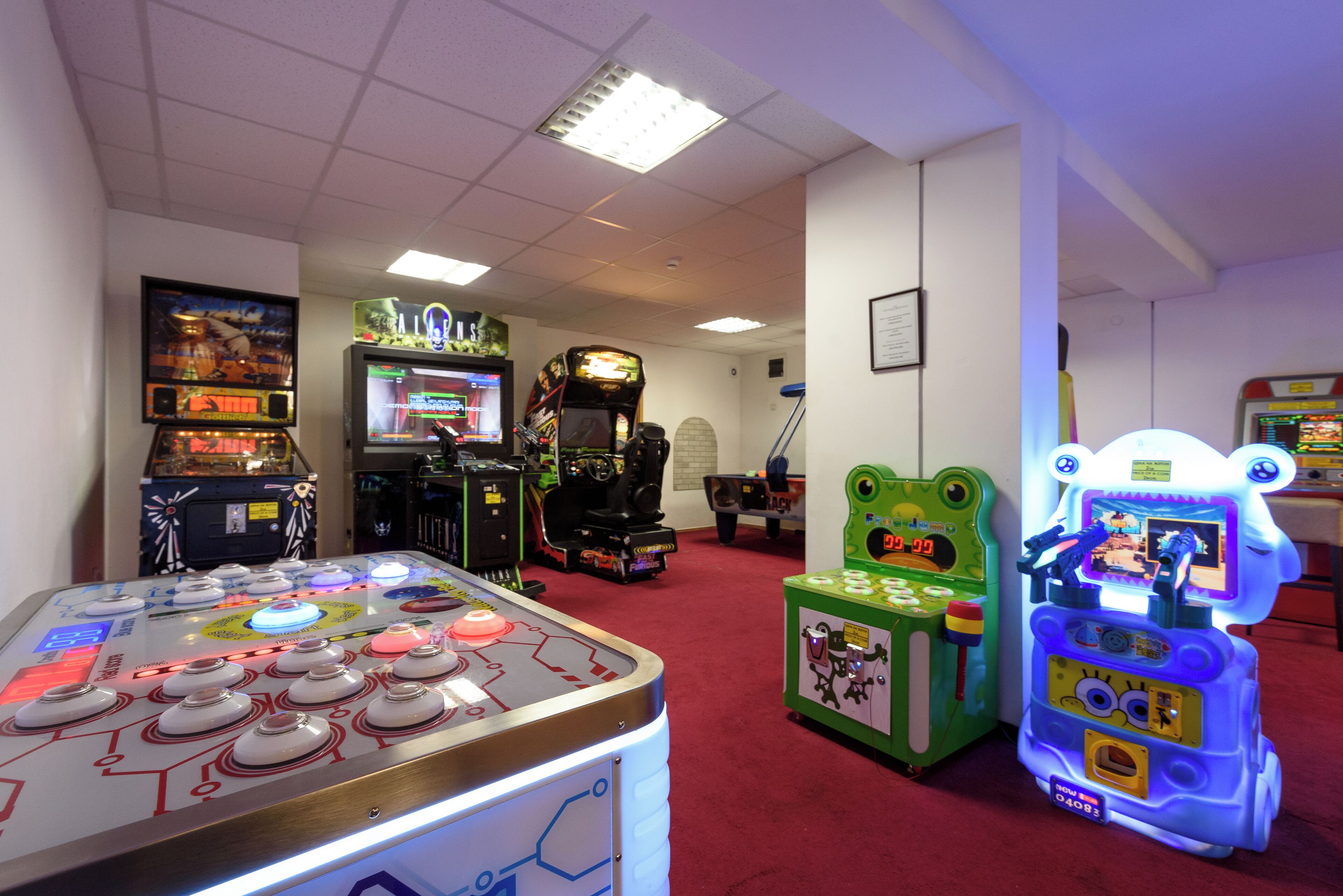 A room with arcade games, including a pinball machine, a racing game, and a claw machine.