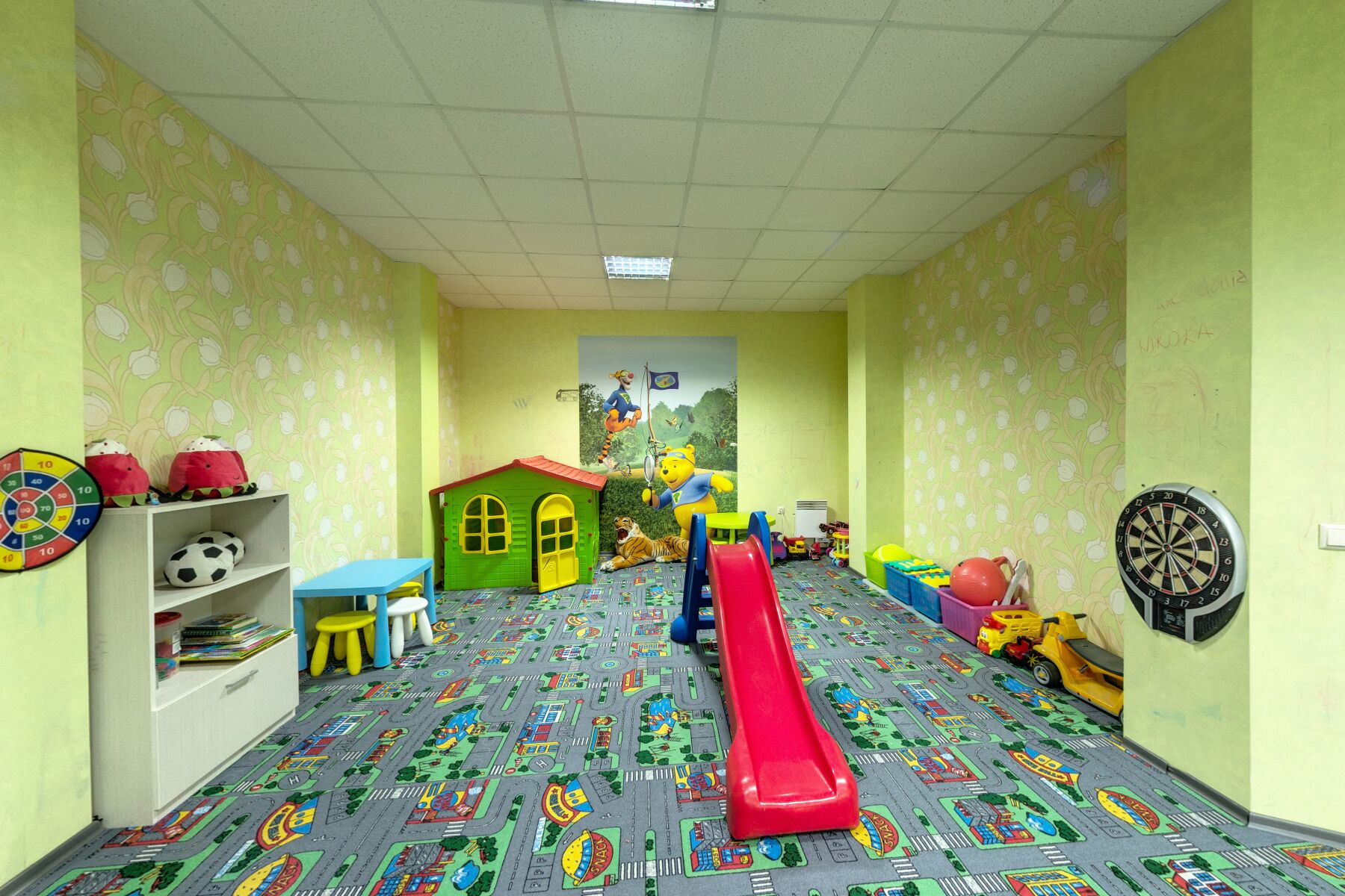 Un cuarto de juegos infantil con un tapete de colores, un tobogán, juguetes y un dardódromo.