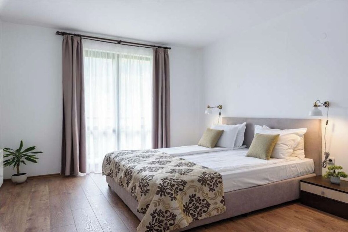 Una habitación de hotel moderna con una cama grande, lámparas de noche, una mesita de noche y una planta en maceta.