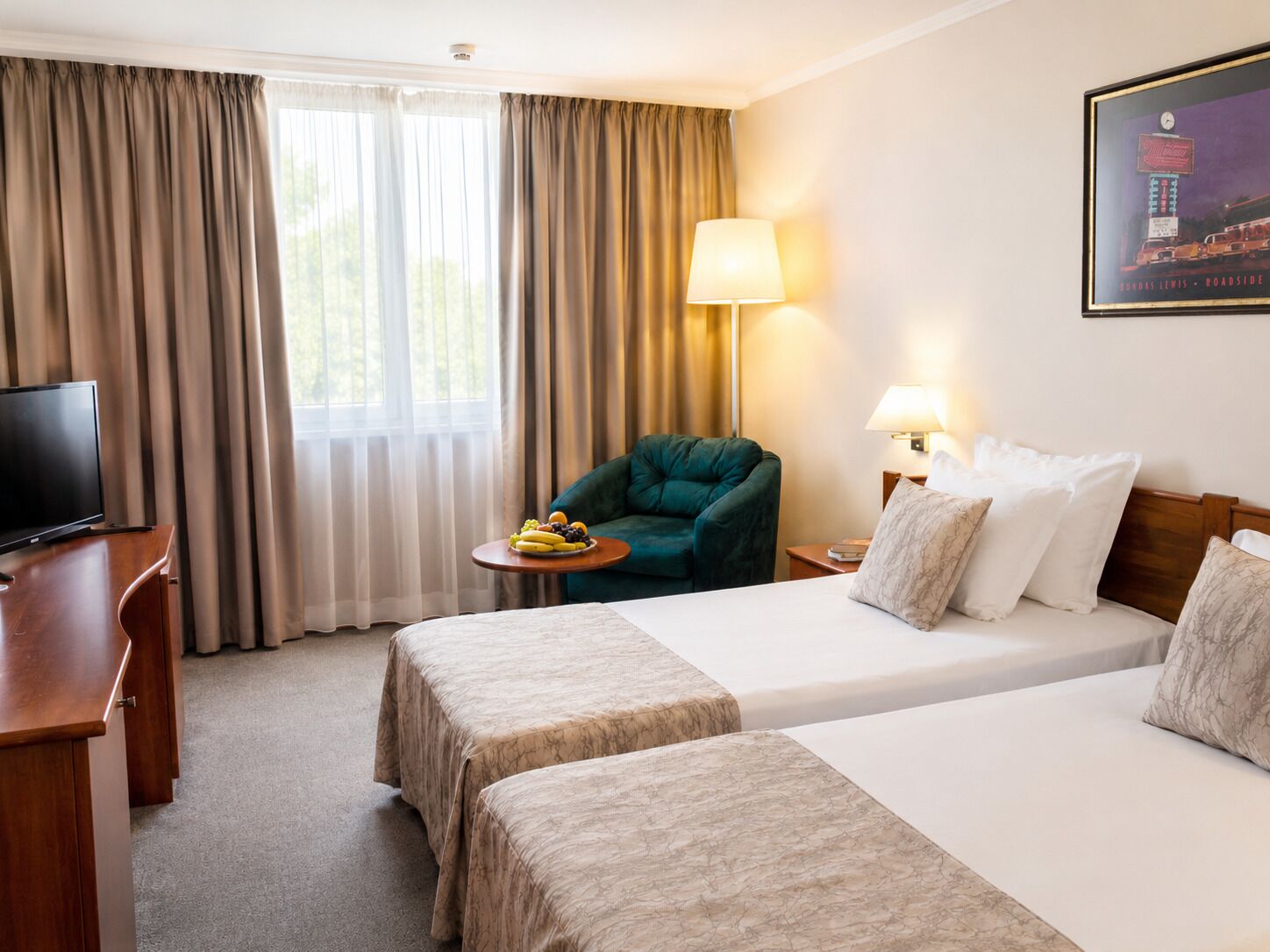 Habitación de hotel con dos camas, un escritorio con televisor, una silla, una mesa con fruta y una lámpara.