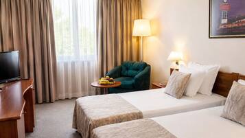 Habitación de hotel con dos camas, un escritorio con televisor, una silla, una mesa con fruta y una lámpara.