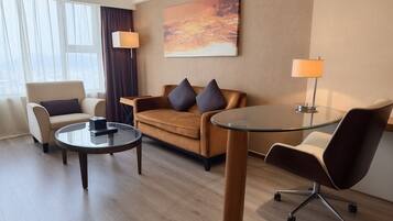 Quarto de hotel moderno com sofá, duas poltronas, mesa de centro de vidro e luminária.