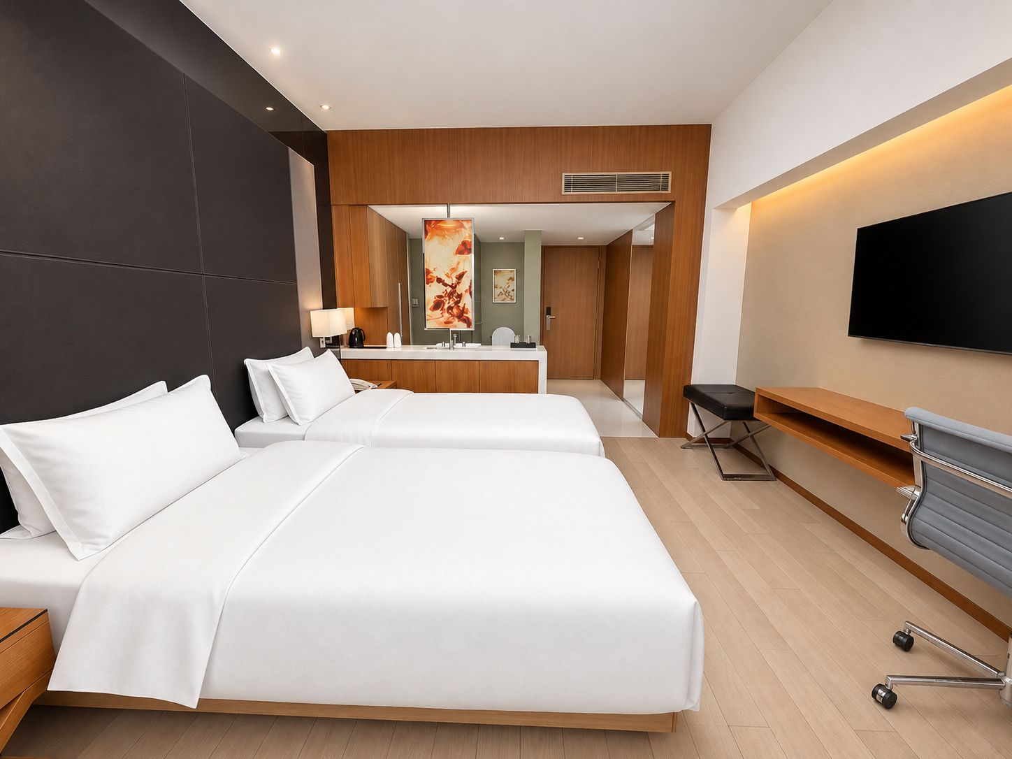 Una camera d'albergo con due letti, una scrivania, una sedia, una TV e un bagno sullo sfondo.