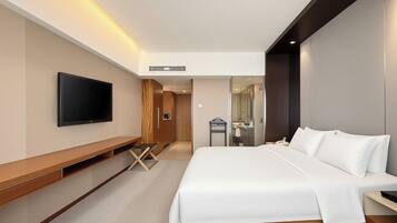 A modern hotel room with a large bed, a flat-screen TV mounted on the wall, a wooden desk, and a walk-in closet.