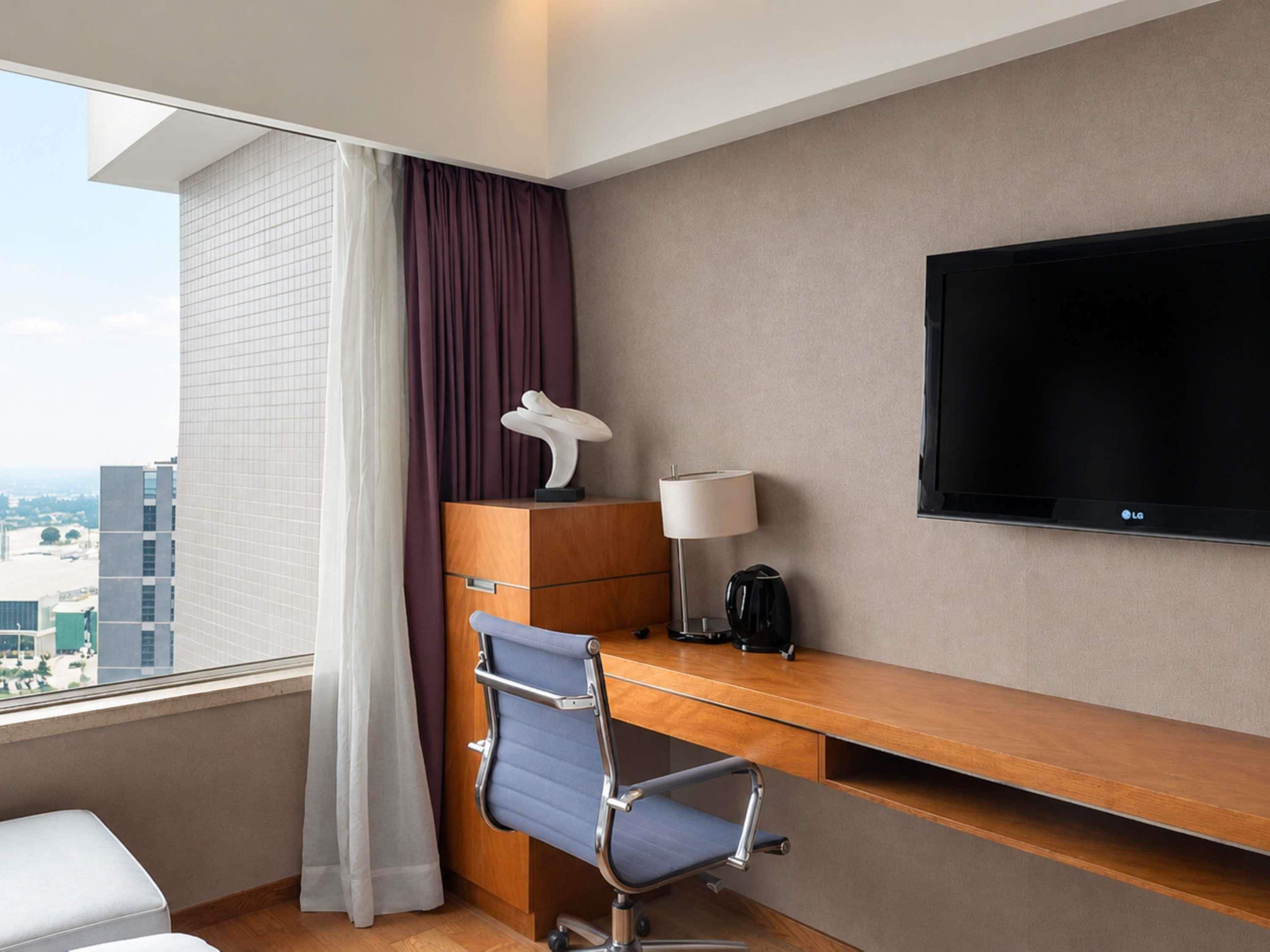 Habitación de hotel con escritorio, silla, televisión y vistas a la ciudad.