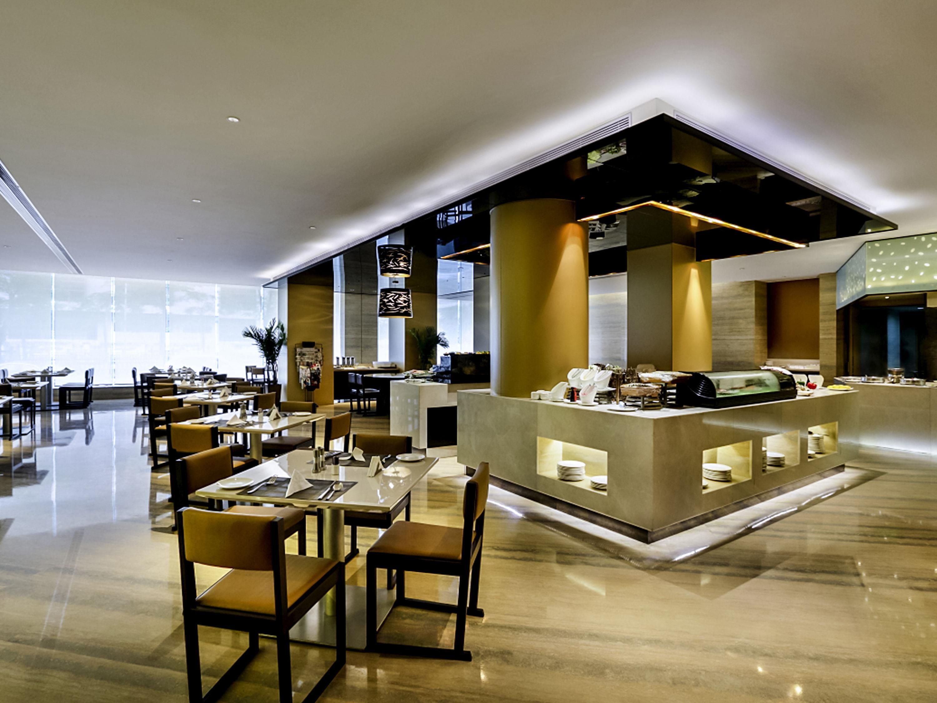 Een modern restaurant met een centrale balie, meerdere eettafels en stoelen.
