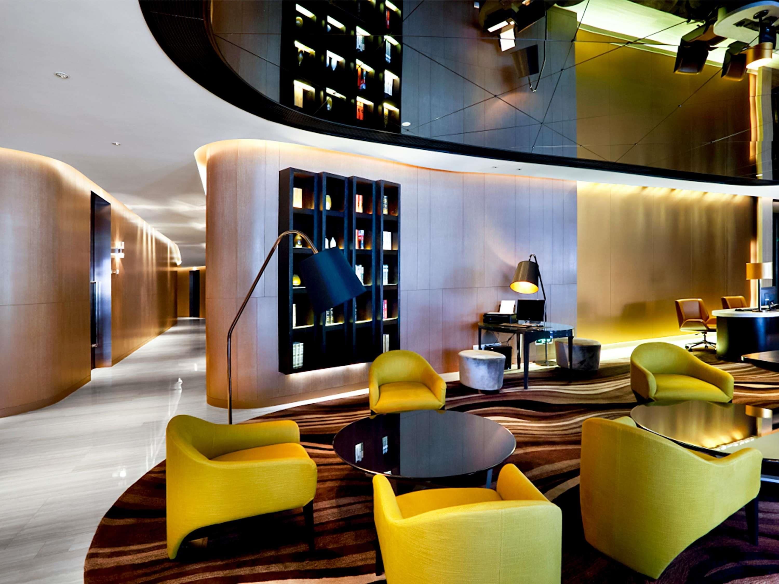 A modern lobby with a curved wall, a seating area with yellow chairs, a round table, and a bookshelf.