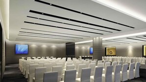 Une salle de conférence avec des rangées de chaises blanches, un grand écran et un pupitre.