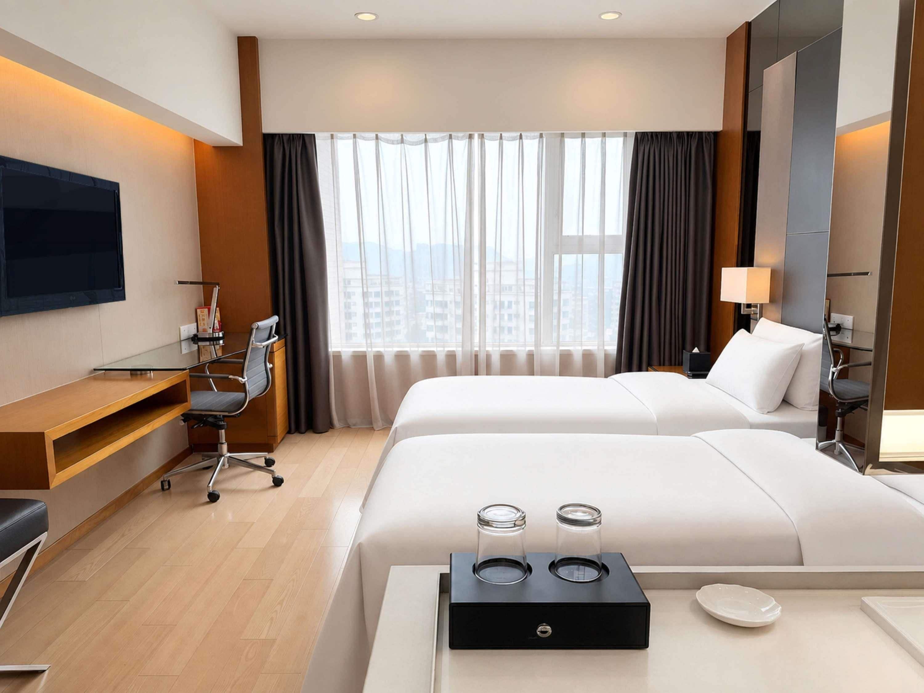 Une chambre d’hôtel avec un lit, un bureau, une chaise, une télévision et une fenêtre avec des rideaux.