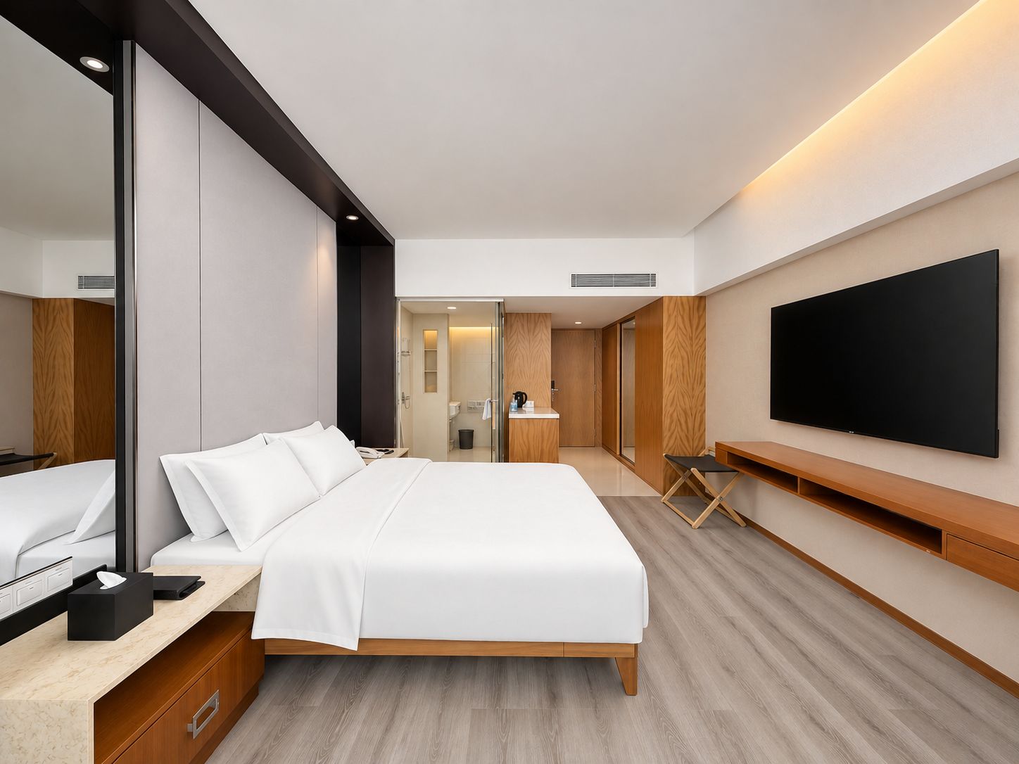 Moderni hotellihuone, jossa on suuri sänky, seinälle asennettu taulutelevisio, yöpöytä ja pieni työpiste.