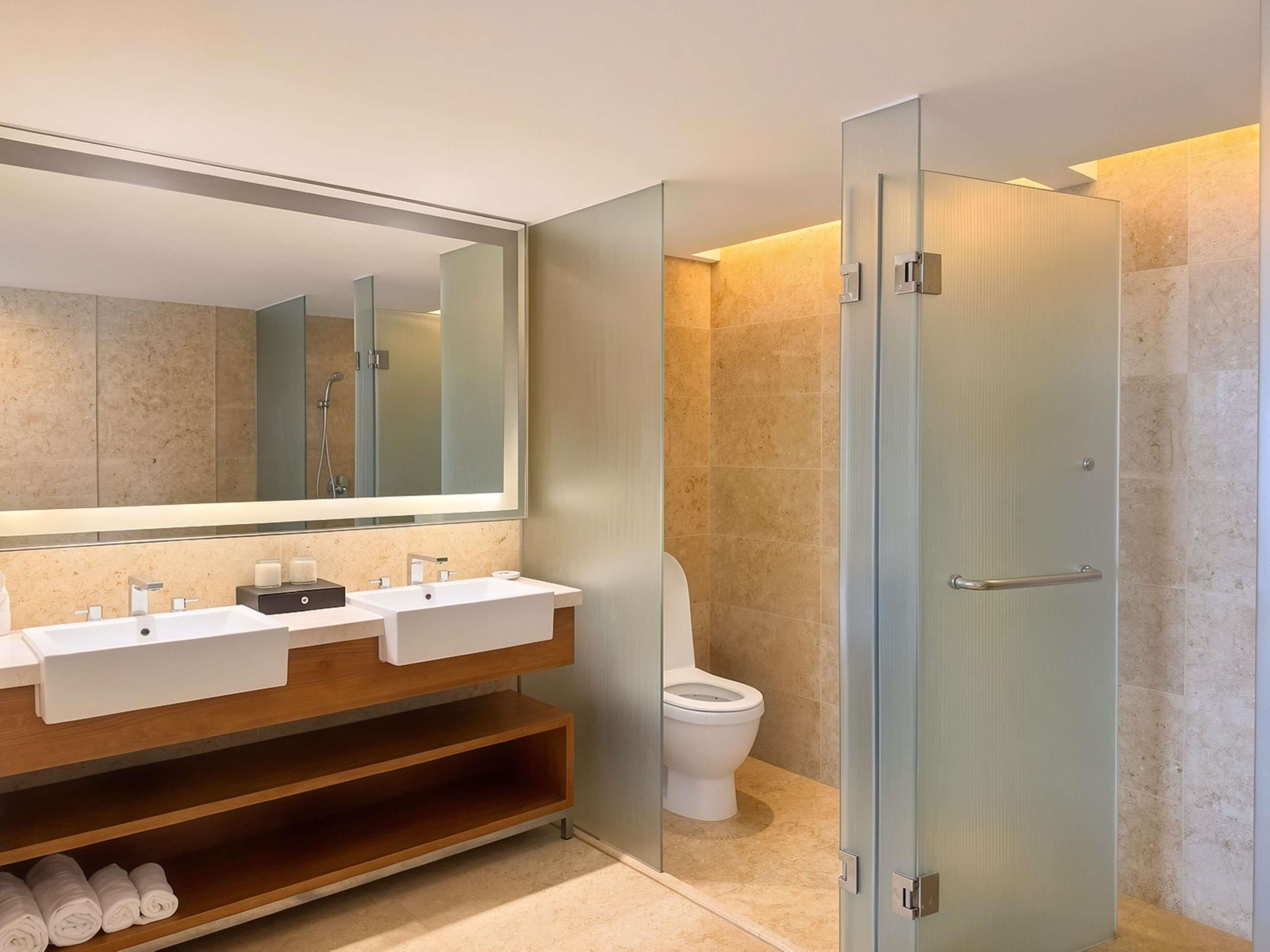 Un baño moderno con tocador doble, un espejo grande, cabina de ducha con mampara de vidrio y un inodoro.