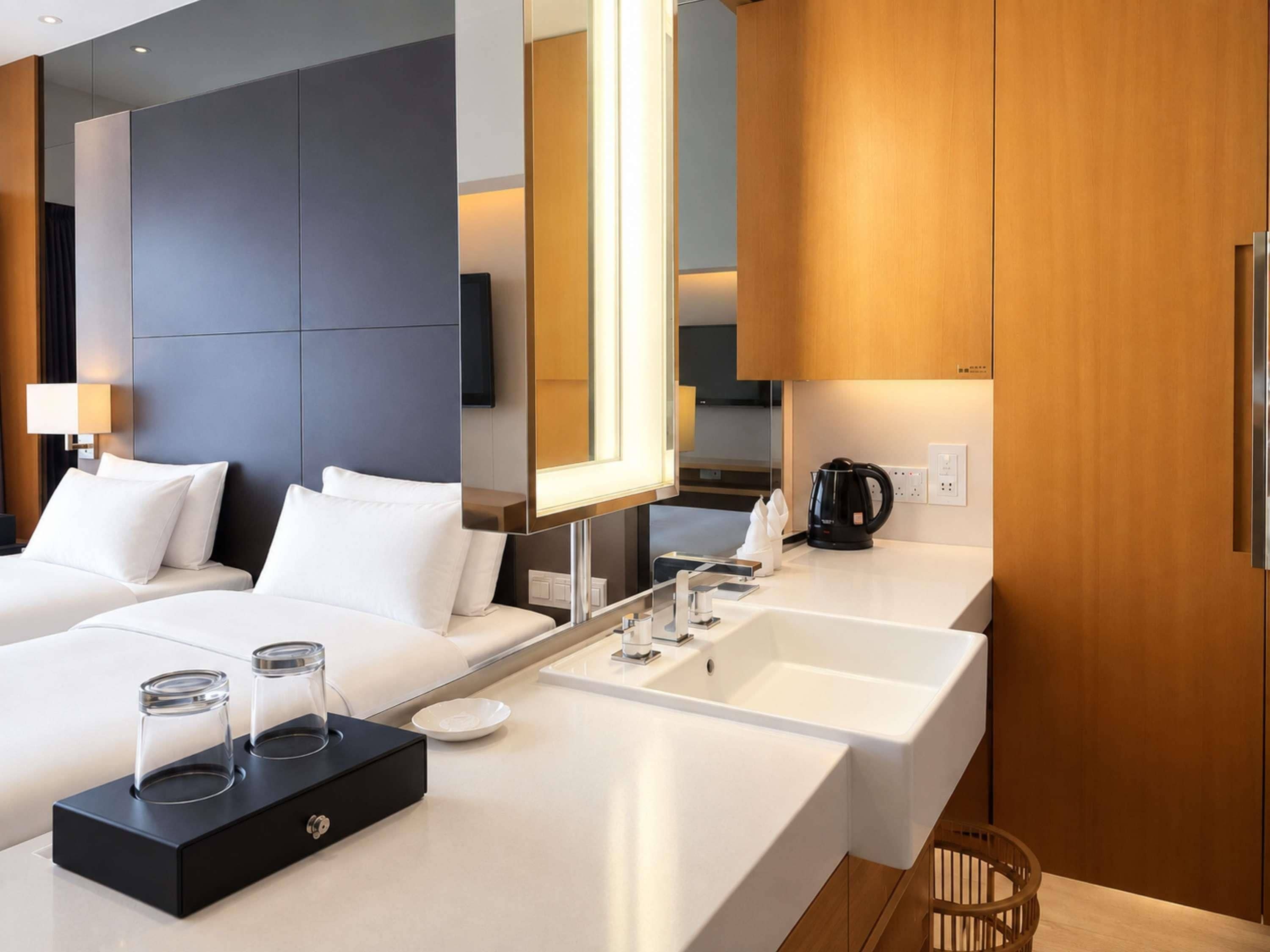 A modern hotel room with a large bed, a separate bathroom with a sink and mirror, and a coffee maker on the counter.