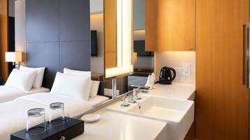 A modern hotel room with a large bed, a separate bathroom with a sink and mirror, and a coffee maker on the counter.