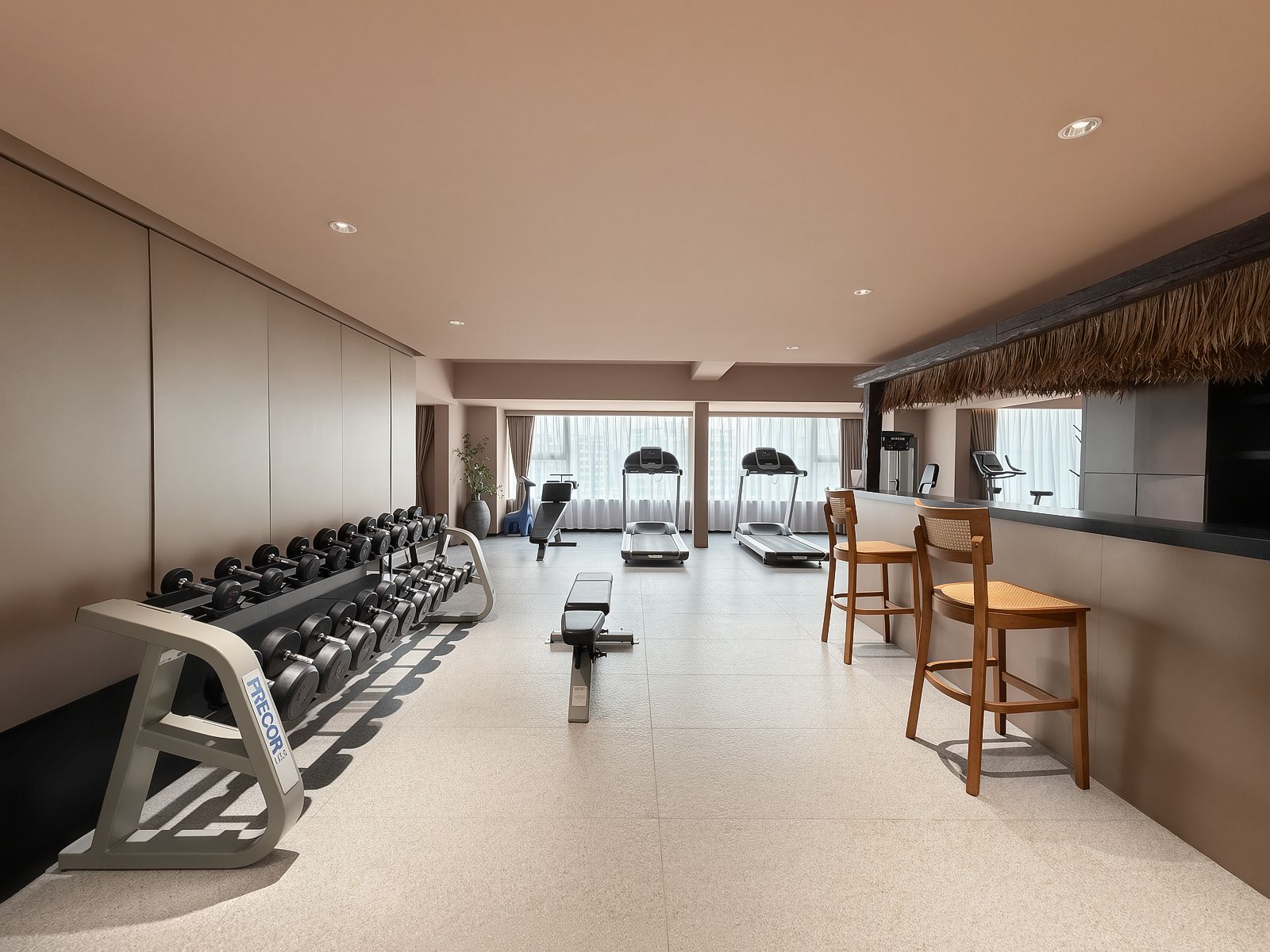 Et moderne hotelgymnasium med træningsudstyr, et siddeområde og udsigt over byen.