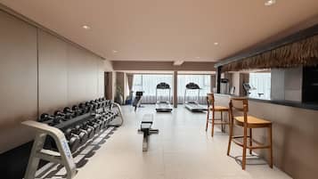 Et moderne hotelgymnasium med træningsudstyr, et siddeområde og udsigt over byen.