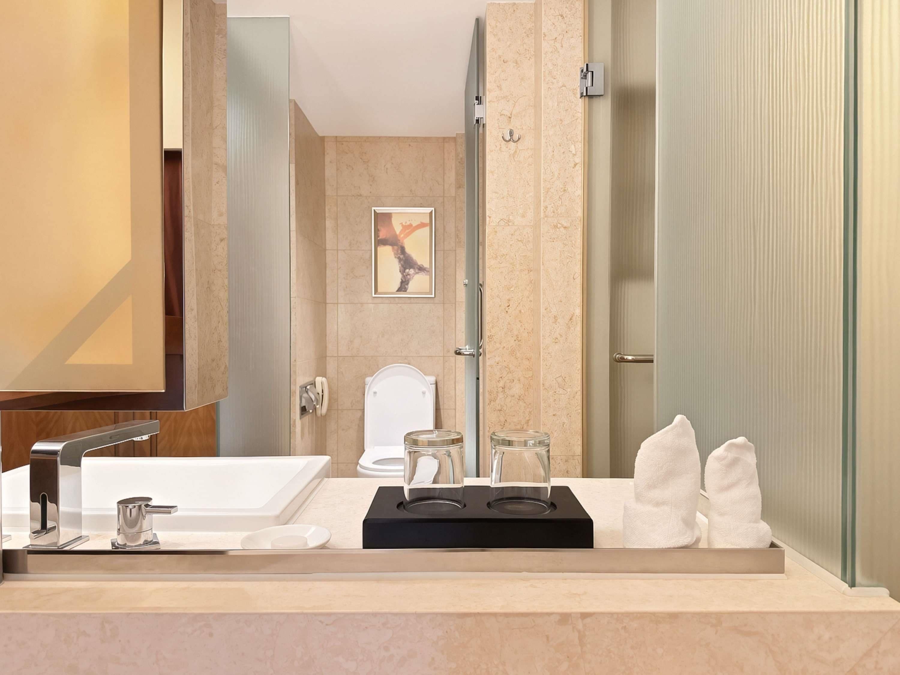 A modern bathroom with a large mirror, a sink, a toilet, and a shower.